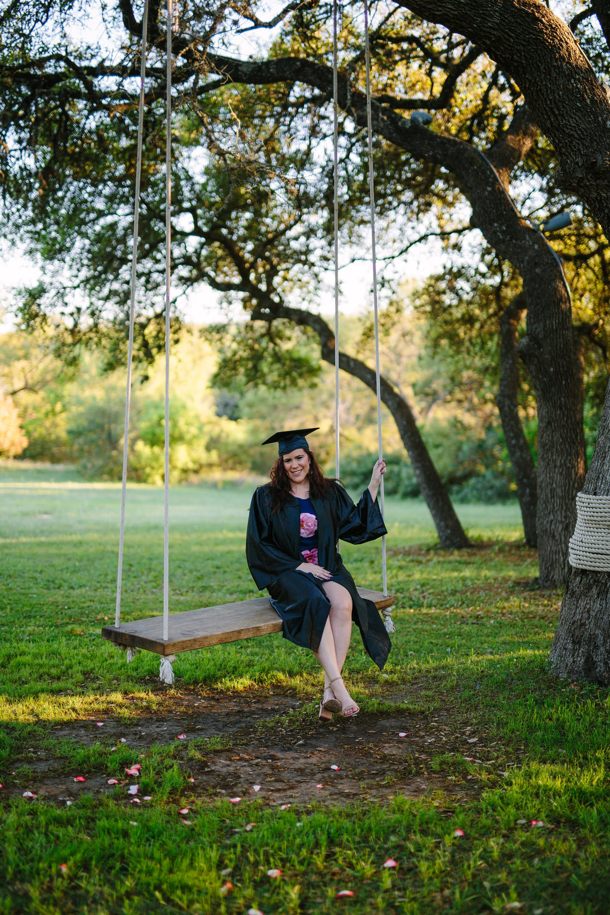 college senior session in cap and gown sitting on swing by San Antonio photographer