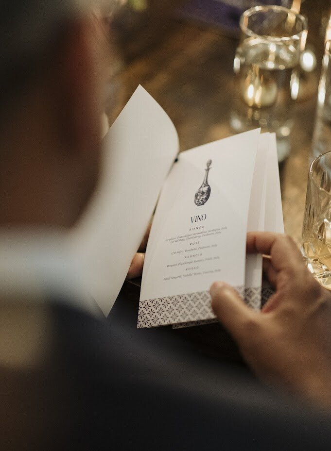 Close-up of an elegant wine list menu, blending modern design with old-world Italian charm at North & Navy in Ottawa. The white menu features navy blue accents and patterns, evoking classic Italian style. This photo captures the essence of an intimate Italian-inspired wedding, with fine details like this Vino menu adding to the ambiance. Perfect inspiration for couples planning an authentic, stylish Ottawa wedding with timeless touches.