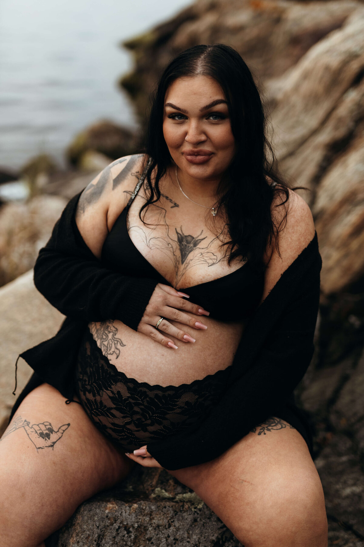 Gravidbild på en gravid kvinna iklädd svarta underkläder sittandes på ett berg ute under en gravidfotografering i Stockholm