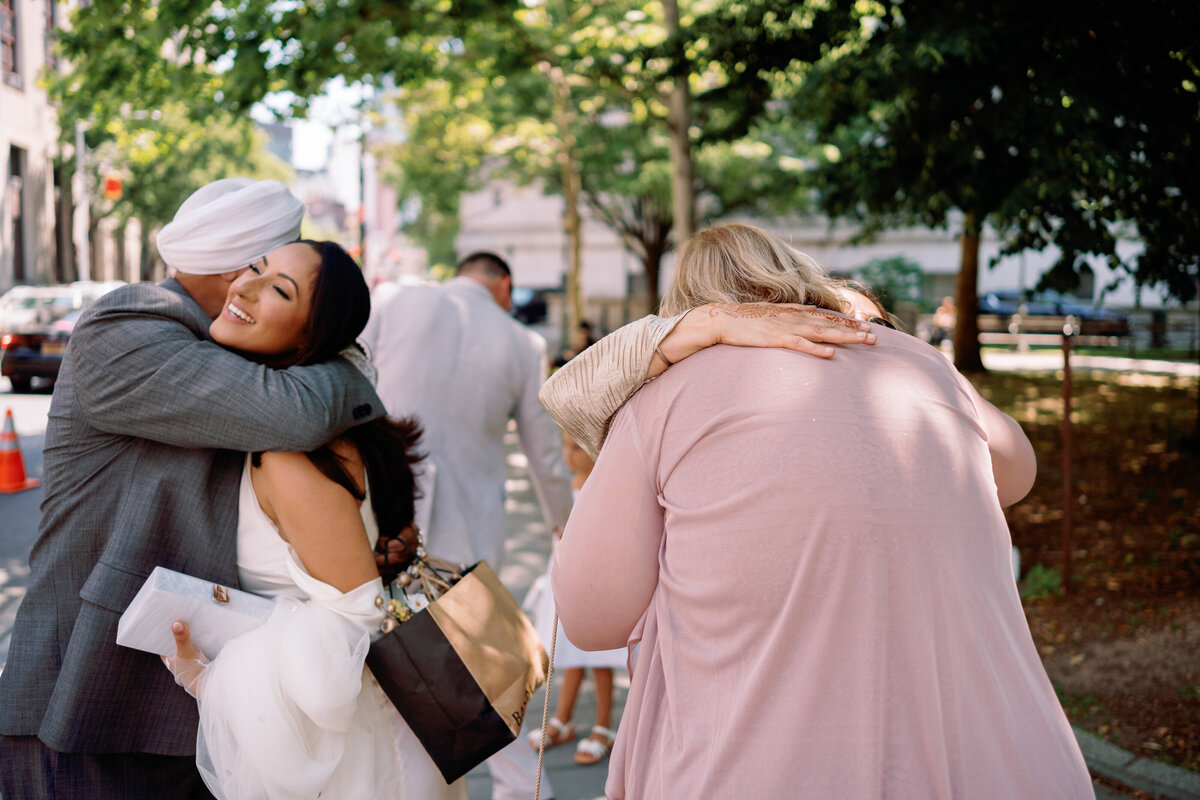 Bride hugging family and friends outside New York City Hall after her intimate elopement with Chris, captured during Japna and Chris’s celebration by NYC wedding photographer Perry Hancock.