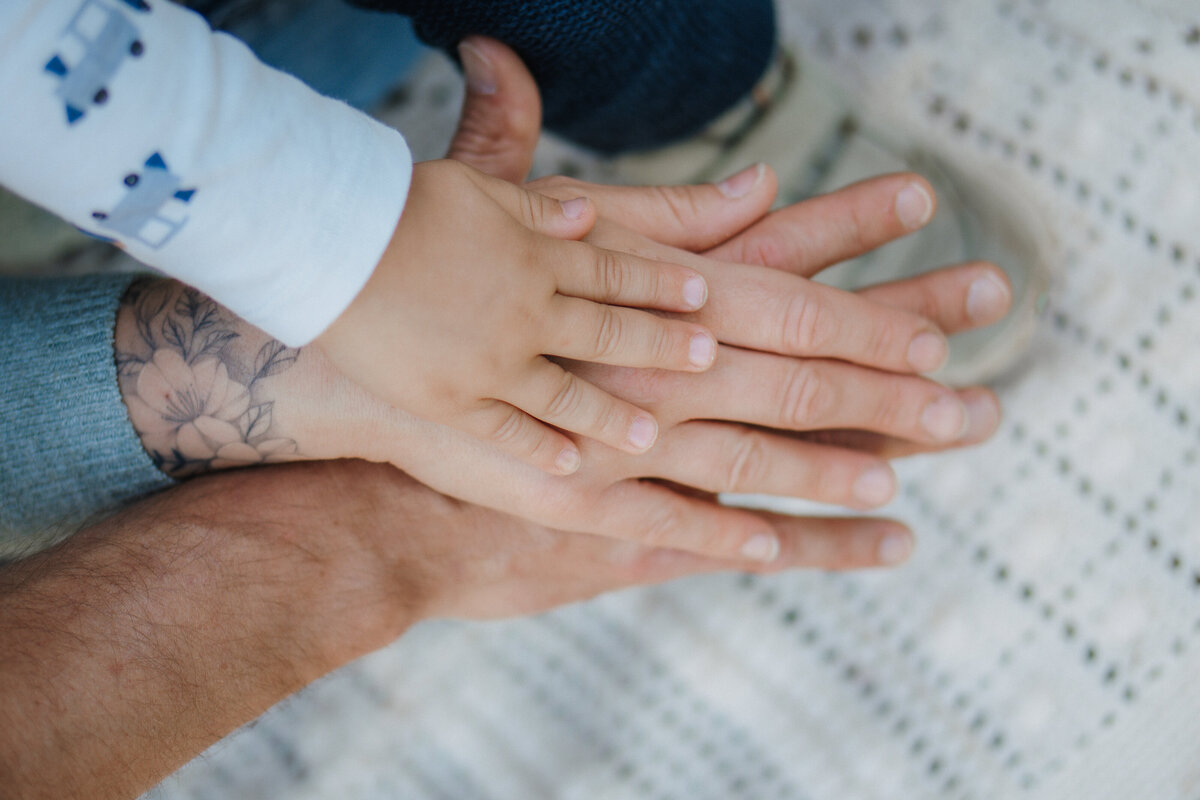 Hände sind übereinandergestapelt. Unten die Hand des Papas, darüber die Hand der Mama und oben die Hand des Kindes.