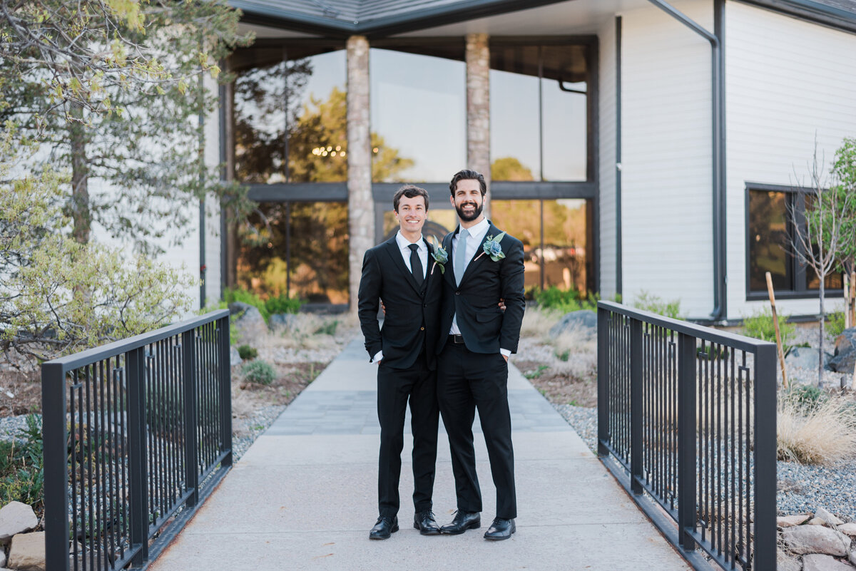 groom and best man stand outside of The Oaks at Plum Creek with their arms around each other