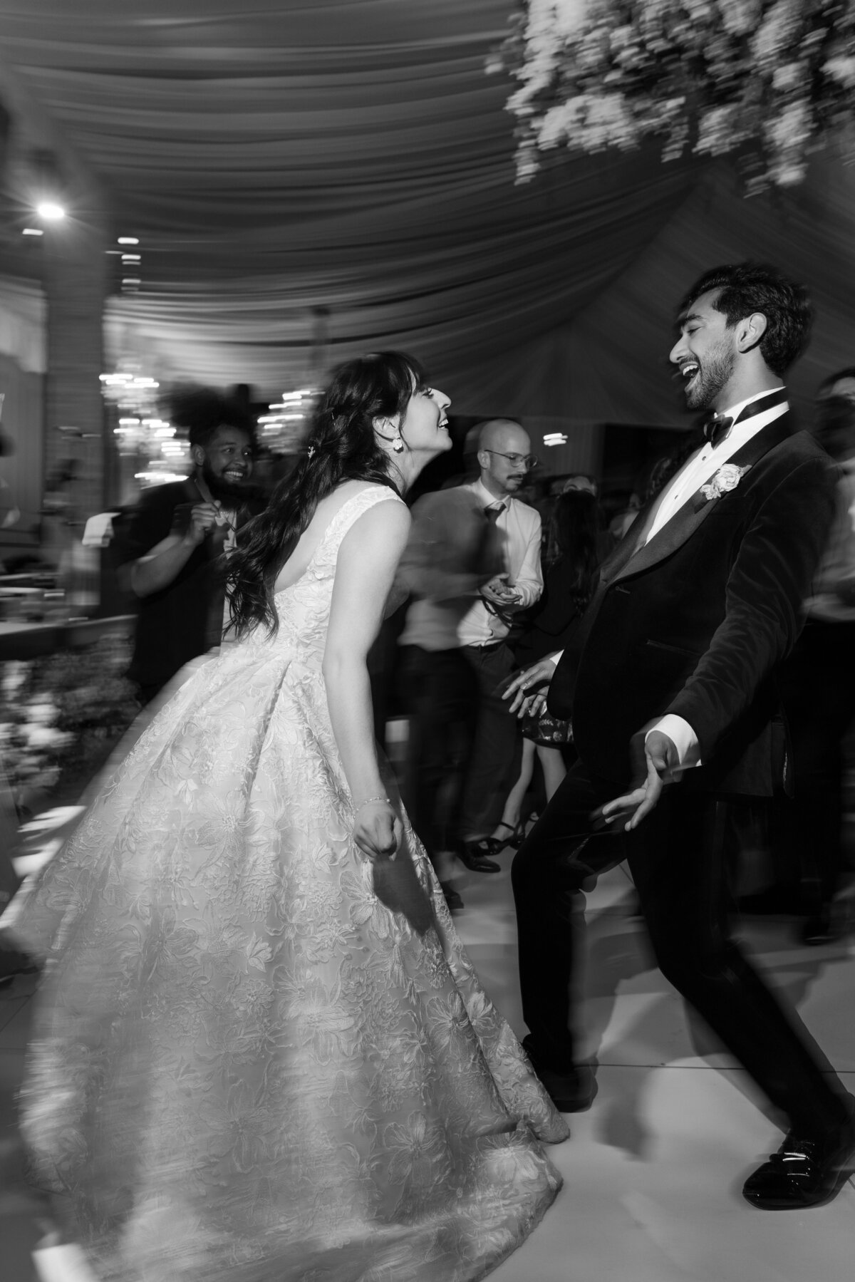 Black and white photo of a couple laughing and dancing during their wedding reception at Water Works in Philadelphia, surrounded by guests and blurred motion from the celebration—capturing the energy, emotion, and movement of a joyful night.