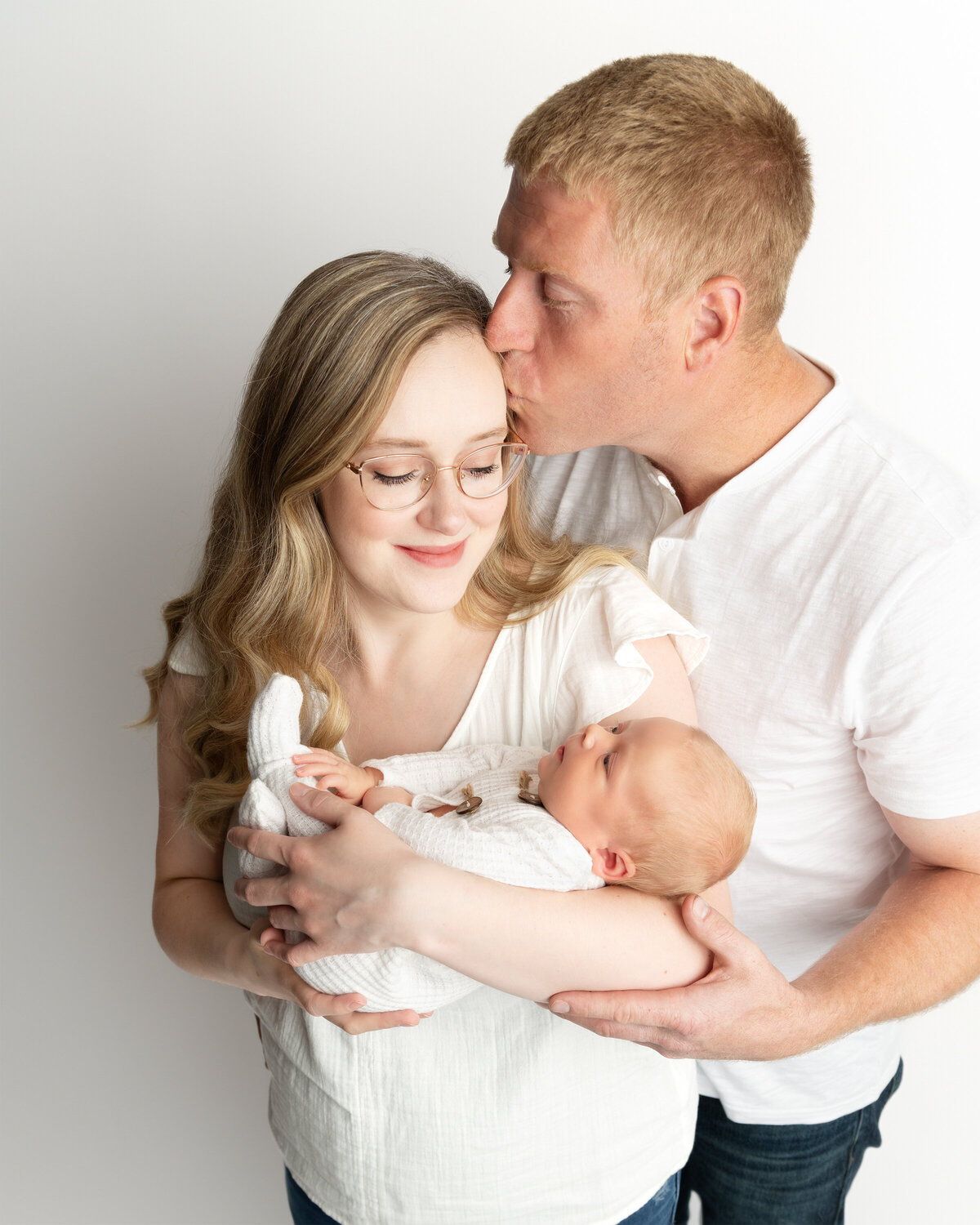 Mother holding newborn son while father kisses her forehead during a newborn family photo in studio in Paris, Ontario