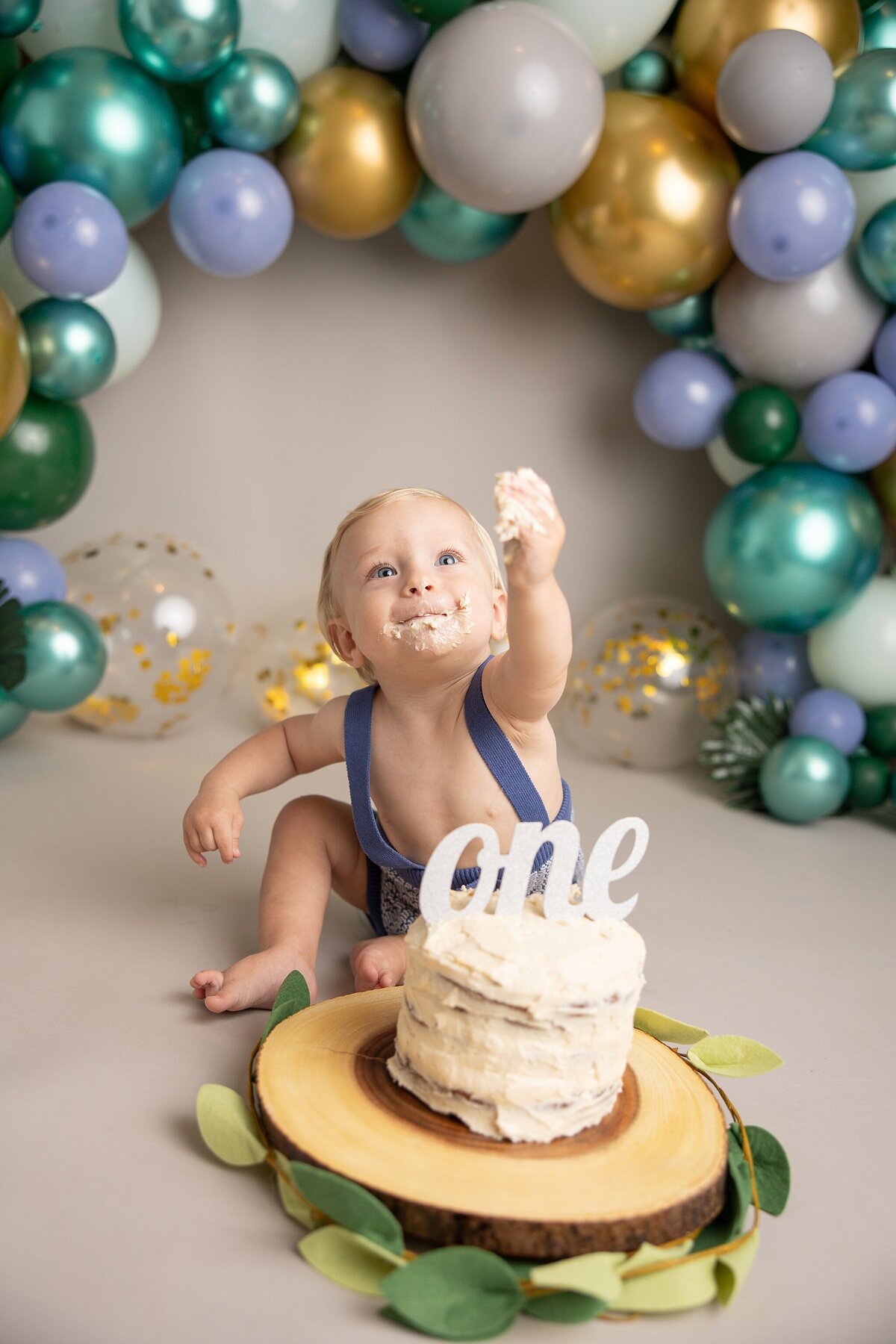 baby boy offering cake to photographer with leaves around cake