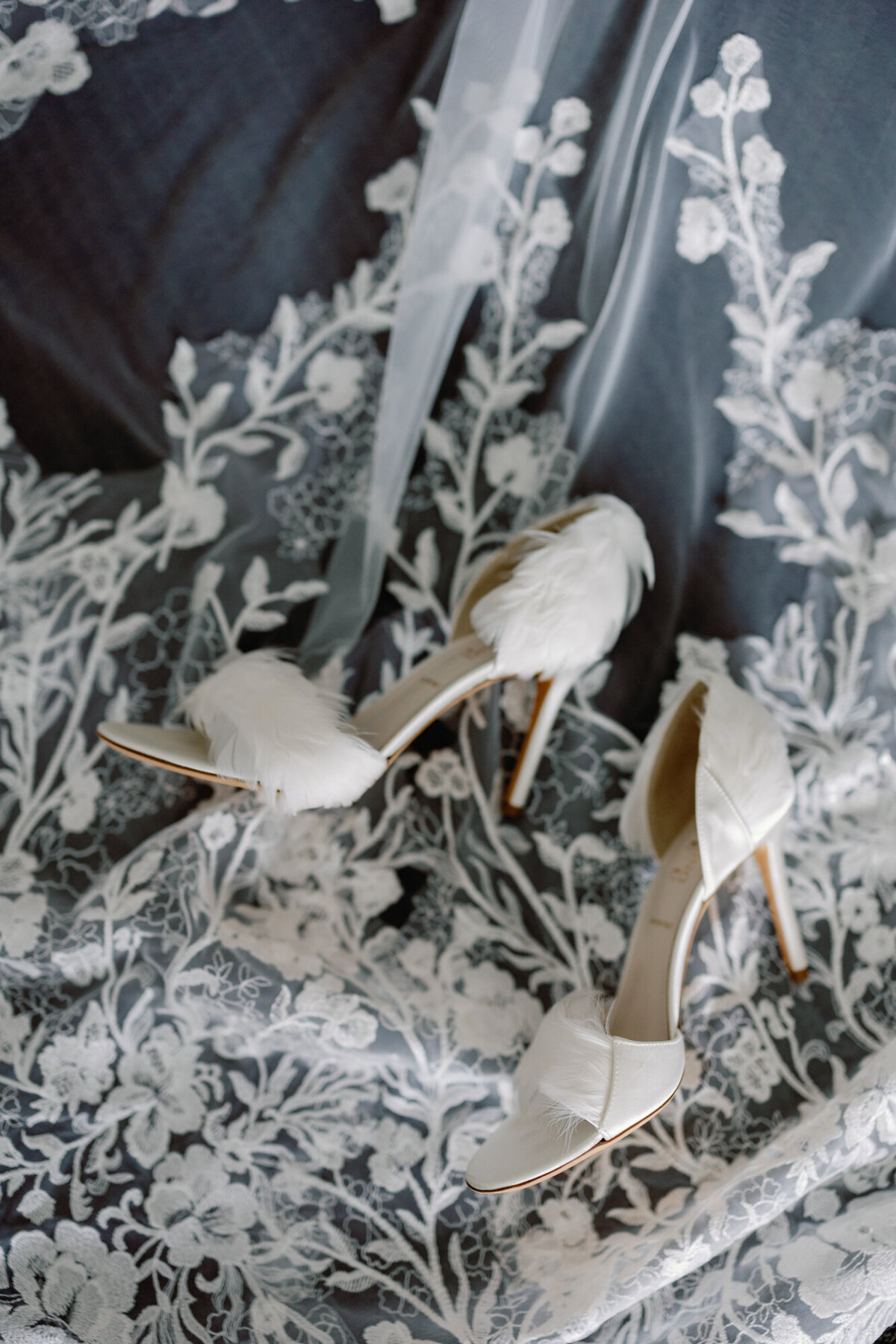 A delicate wedding detail shot of elegant bridal shoes resting on a flowing veil.