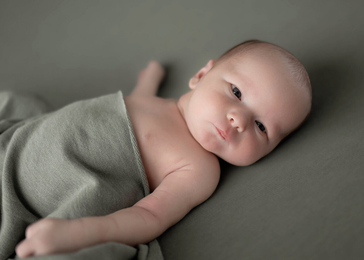 A newborn baby lays with eyes open on a green pad