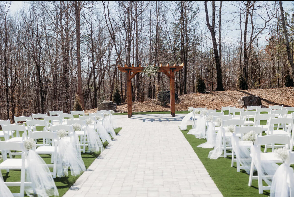 outdoor wedding set up with white chairs and tool with a beautiful arbor