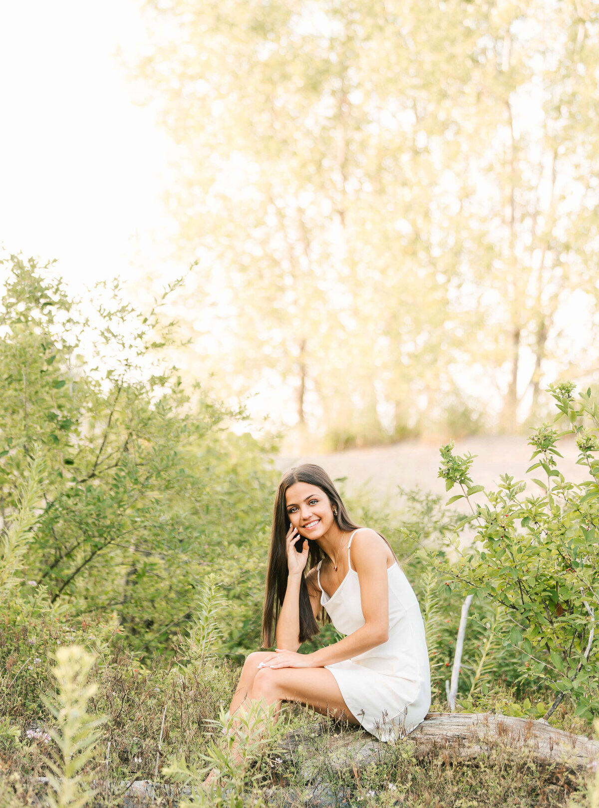 Senior photo of a girl sitting on a log in a white dress in Erie Pa