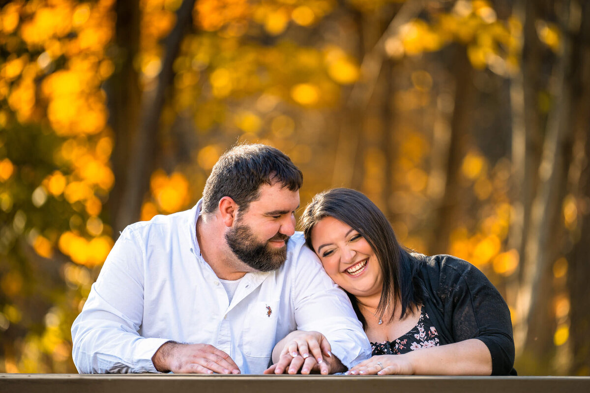 Engagement portrait of couple smiling and snuggling next to each other on a park bench at their engagement session in brush creek park, beaver county, PA. Captured by Pittsburgh Engagement Photographer Michael Fricke Photography.