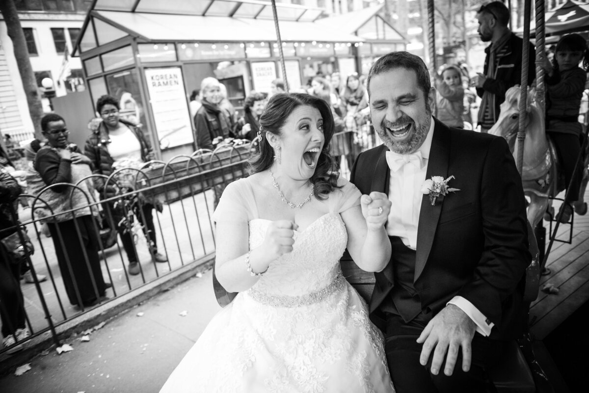 A bride and groom laughing as they ride a merry-go-round.
