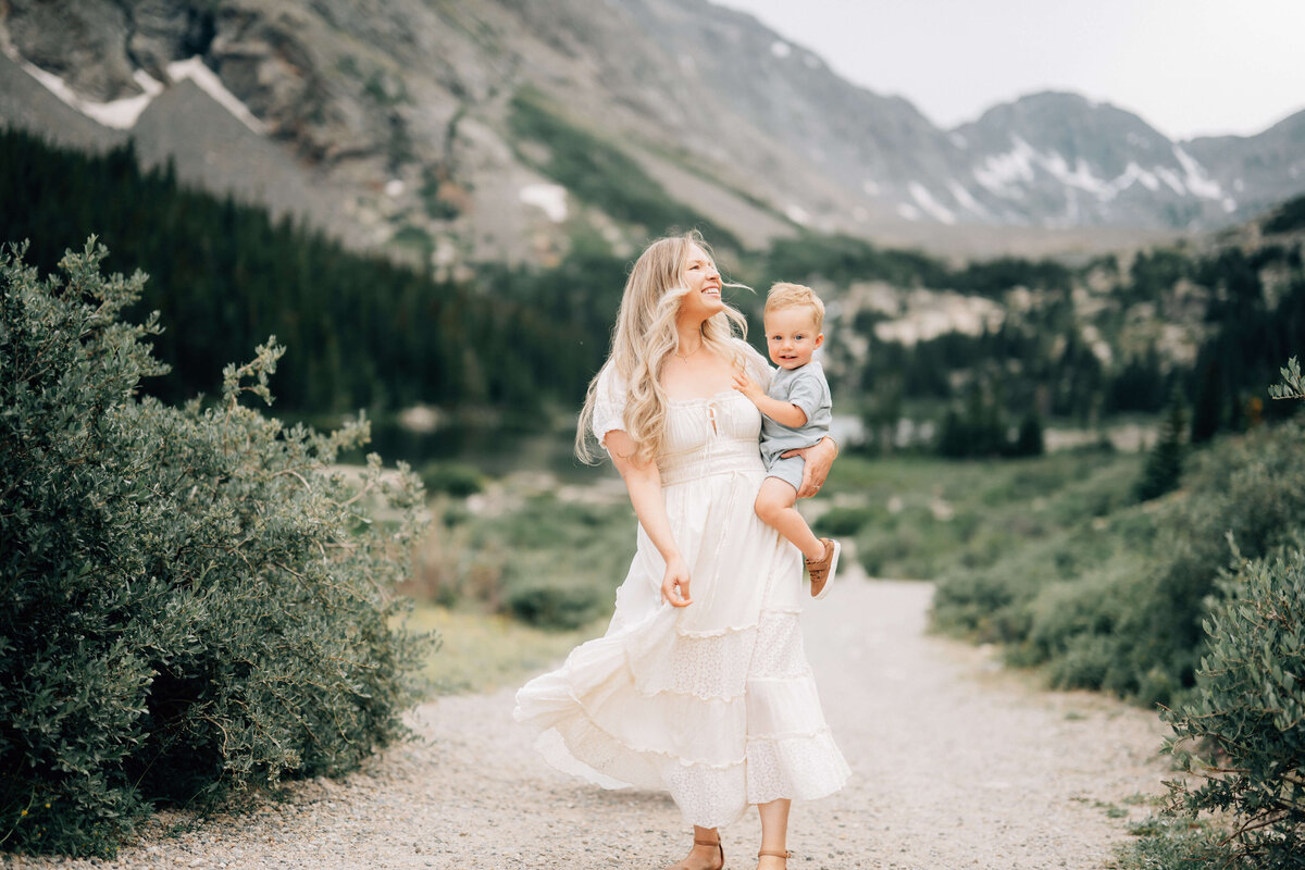 mom walking along a trail in the mountains holding her toddler boy and twirling her dress