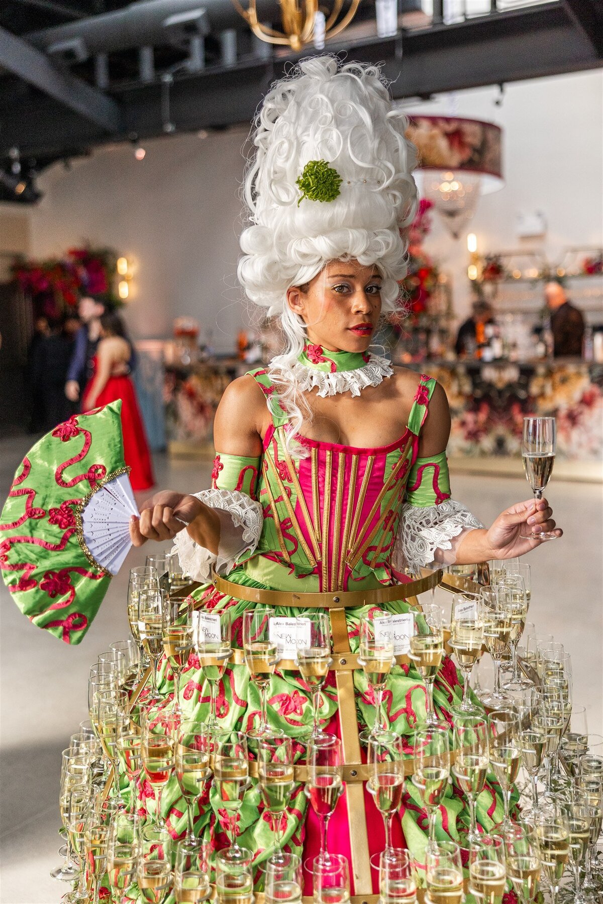 Large gathering at a Baroque-themed event, with guests dressed in formal attire mingling amid lavish decor including gilded furniture, crystal chandeliers, and rich drapery in a grand, ornately detailed space