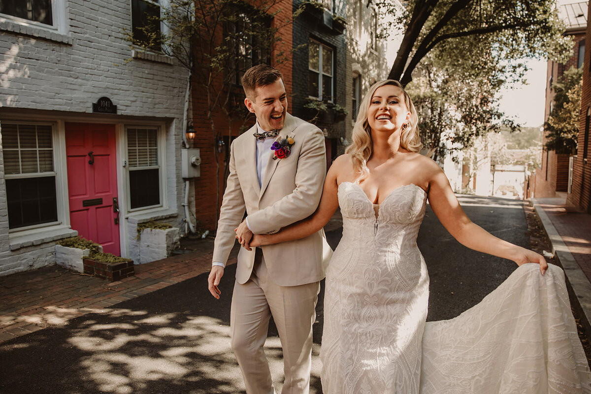 Newlyweds laughing and holding hands as they walk down a road 