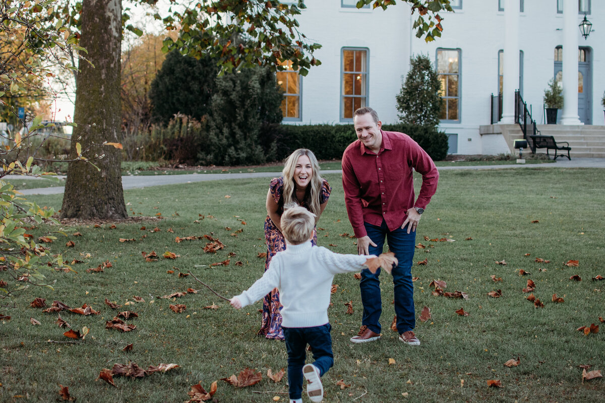 mom and dad smiling at their son running towards them during a joyful outdoor family photoshoot