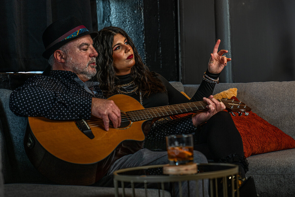 Two people sitting together while one plays guitar 