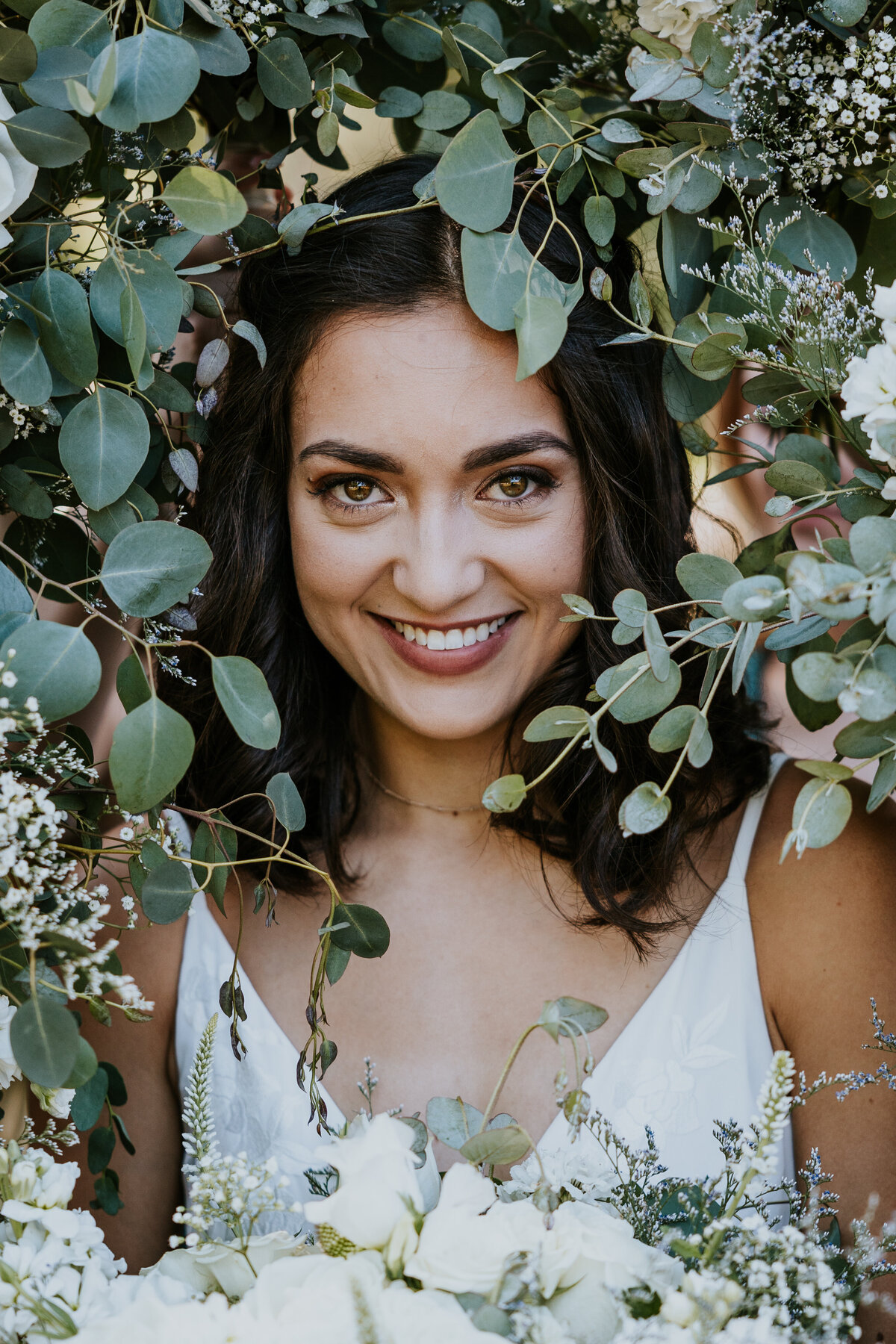 Bride smiles looking at camera while bouquets of flowers surrounding her face.