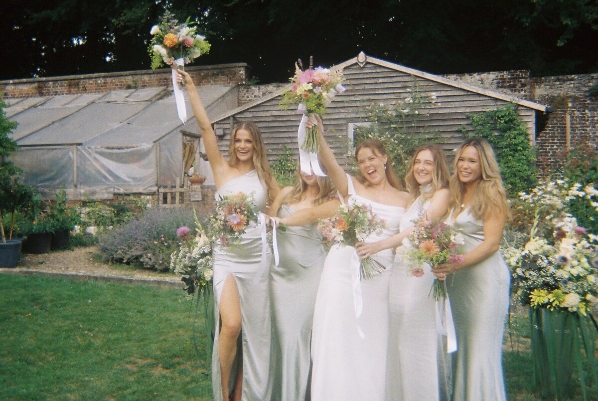 Bridal party holding their bouquets of flowers up high, smiling