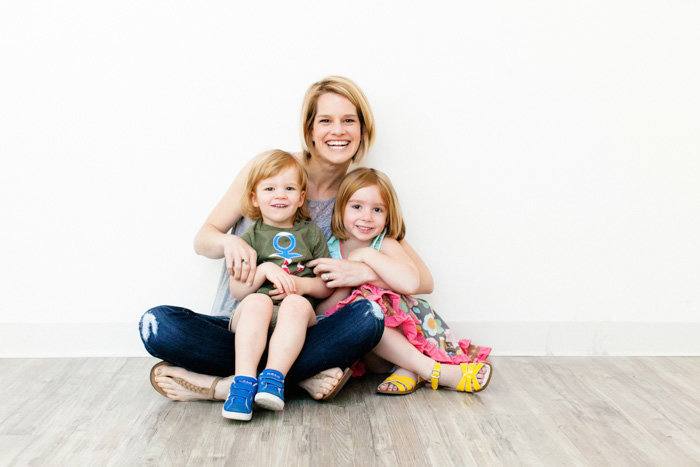 In studio portrait of mom sitting on the floor with two children in her lap
