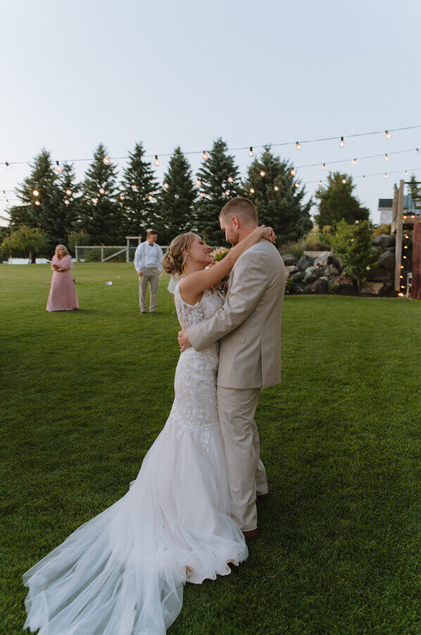 A bride and groom doing their first slow dance at their wedding reception on a grass lawn.