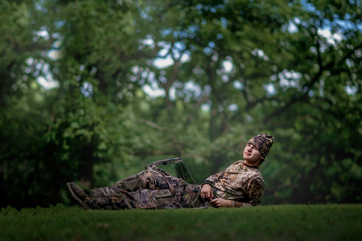 A Knoxville high school Iowa senior hunter lays in a lawn in camo with his hunting bow