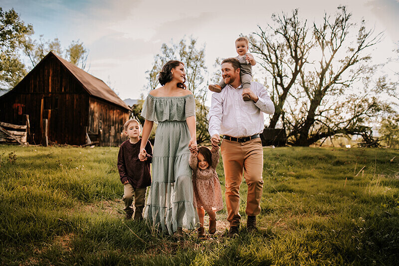 Family of five walking and holding hands while looking at each other and youngest infant son rides on dad's shoulders