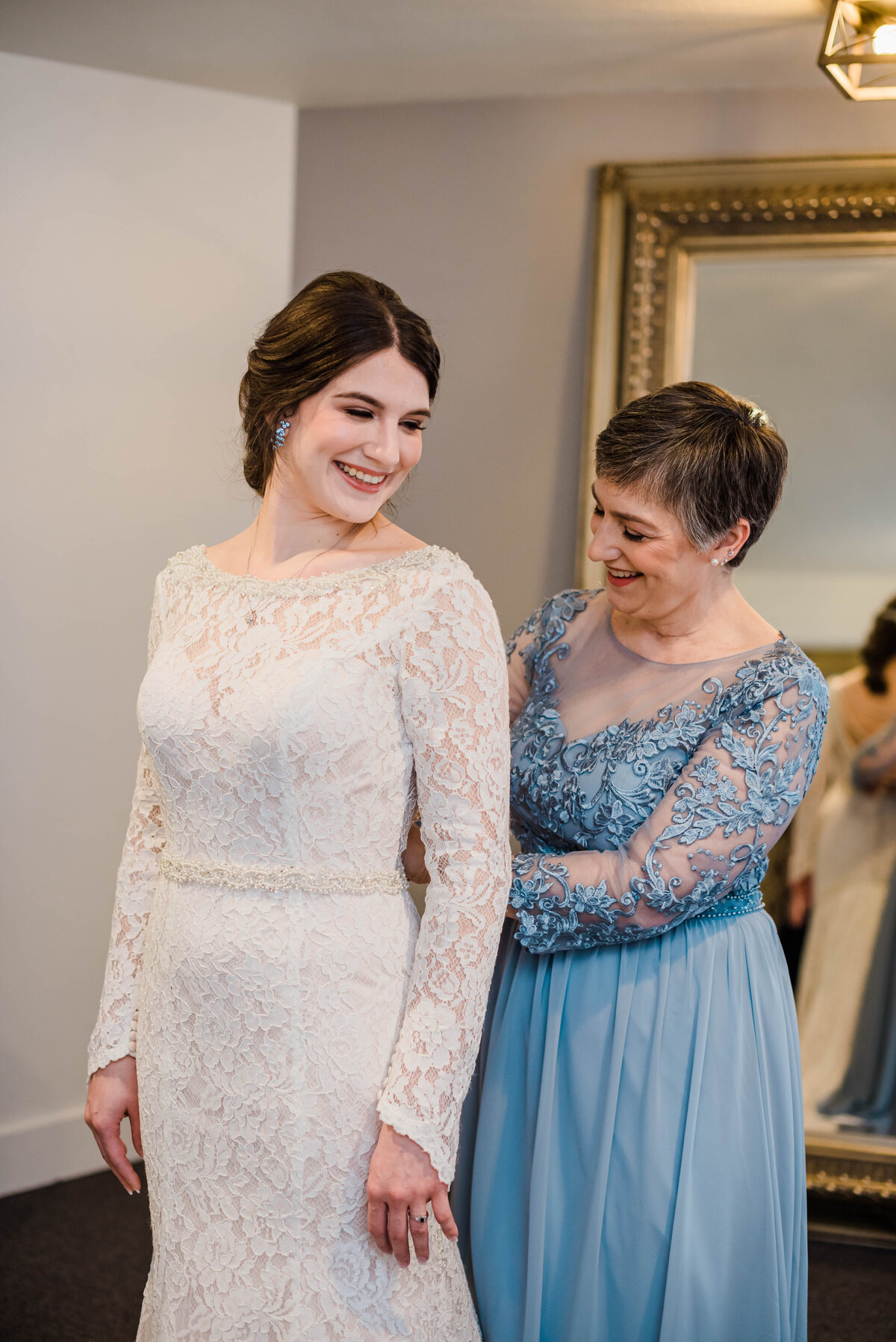 Mom buttons up the back of a bride's dress as she gets ready for her wedding at boulder wedgewood