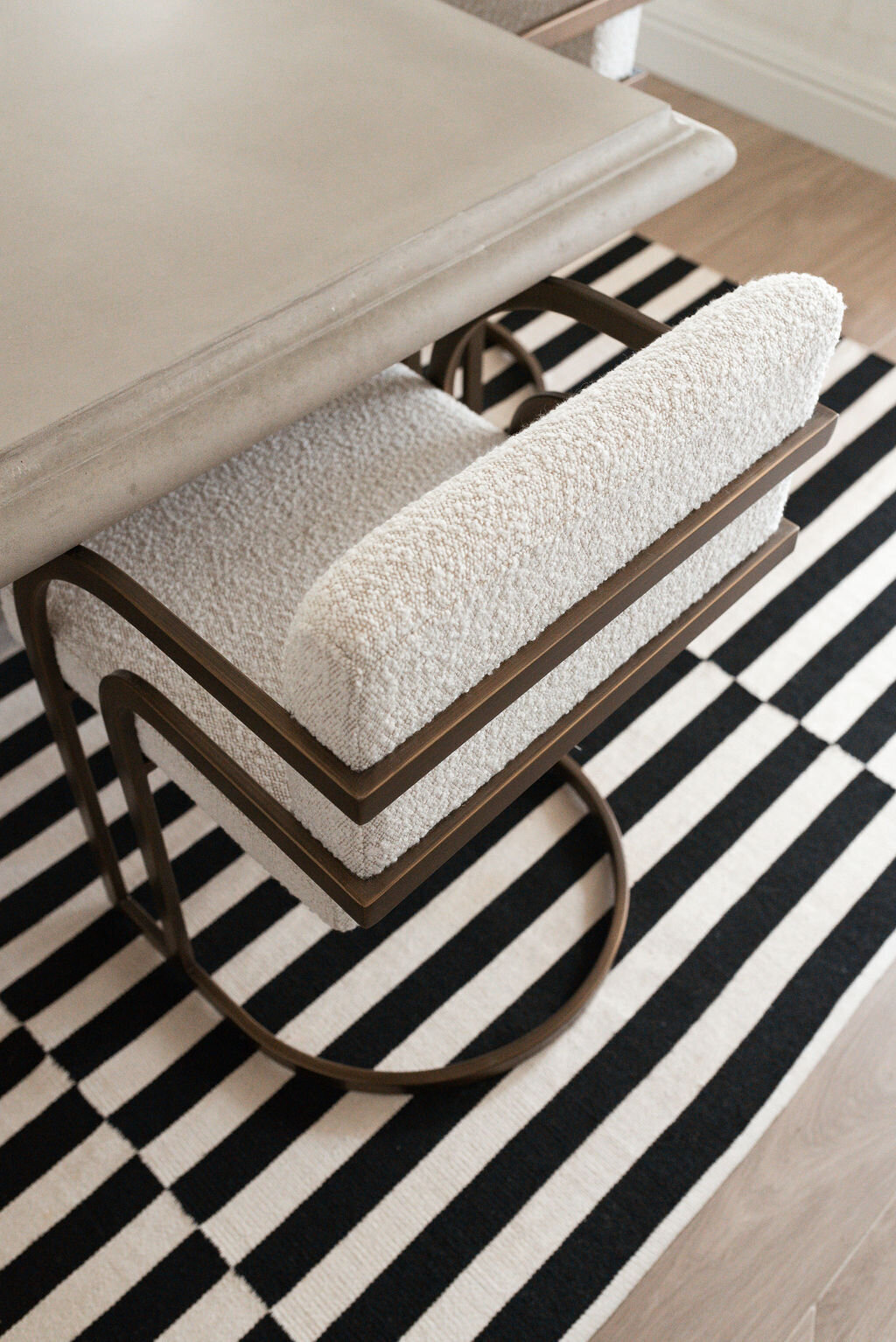 A white cushioned chair pulled up to a neutral dining table, sitting atop a black and white striped rug.