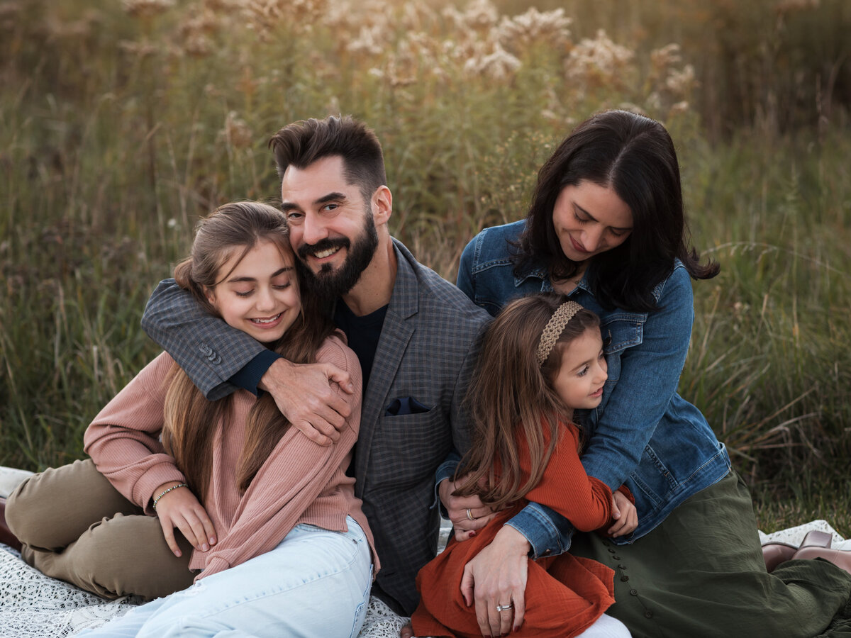 mom dad and two daughters posing in field for family photos