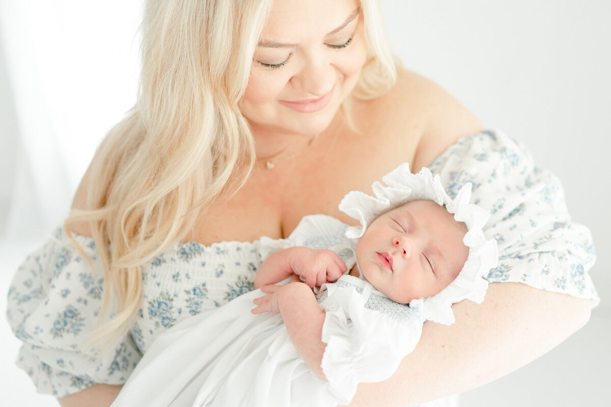newborn in a white bonnet is held by her mother In Kristie Lloyd’s Nashville newborn photographer studio