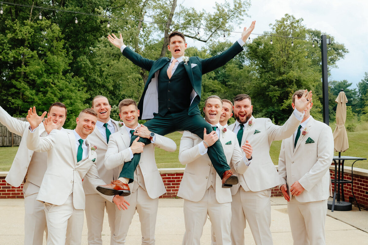 Groomsmen holding the groom on their legs posing together at Aurora Meadows.