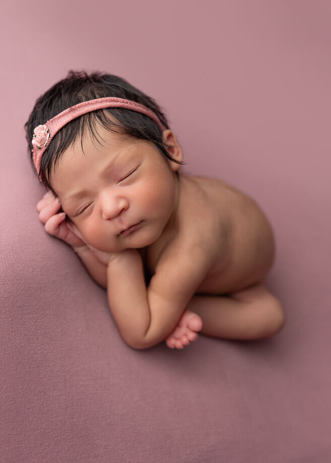 newborn baby girl posed nude on a dusty rose backrop and a matching headband