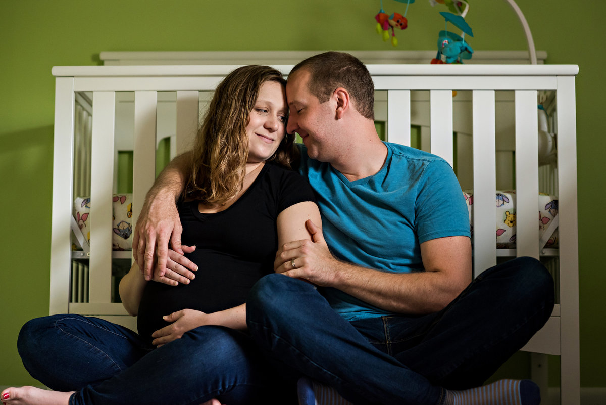 A newly pregnant couple sit against the babies crib in their home maternity session.