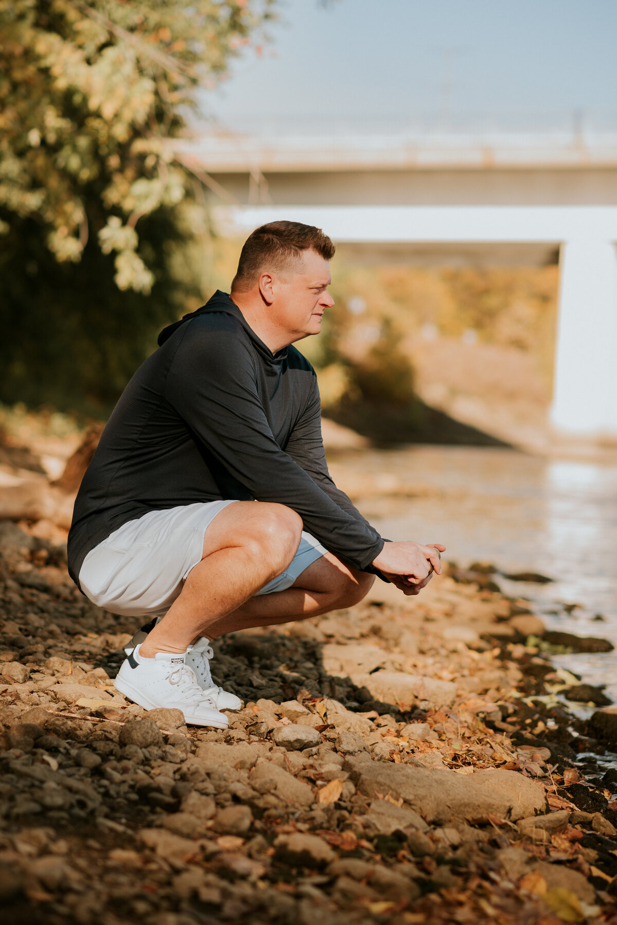 Active dating profile image of a man in athletic shorts crouching near a riverbank in Minneapolis, ideal for apps like Bumble and Hinge.