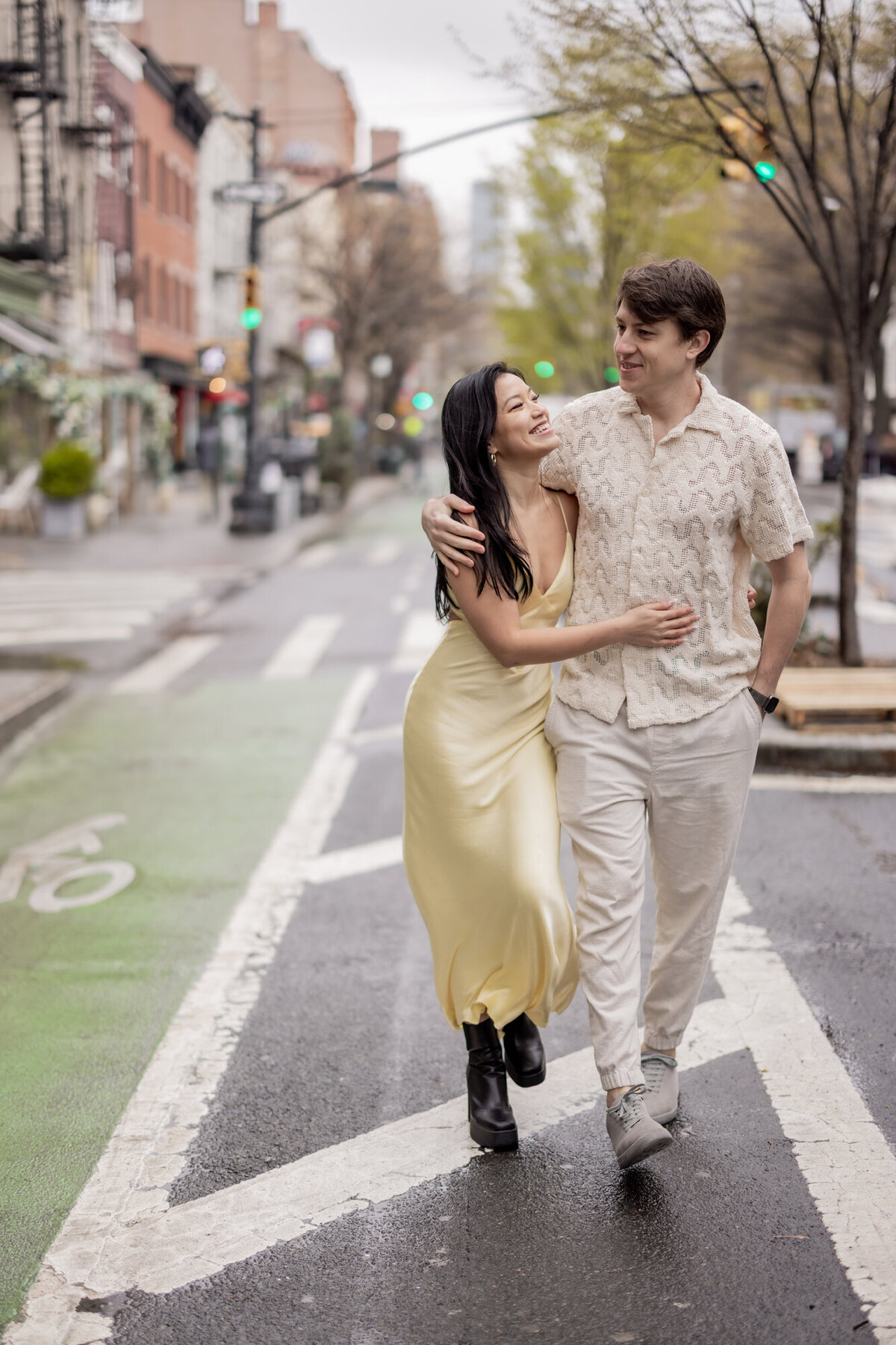 Couple walking arm in arm through the West Village in NYC during their engagement session, smiling and enjoying a quiet moment on a rainy spring day.