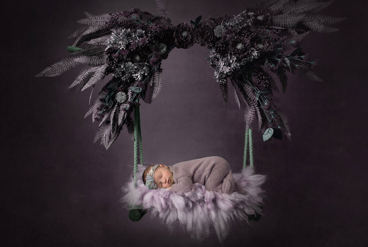 A Pella Newborn Photographer image of a newborn baby sleeping in a swing in a studio