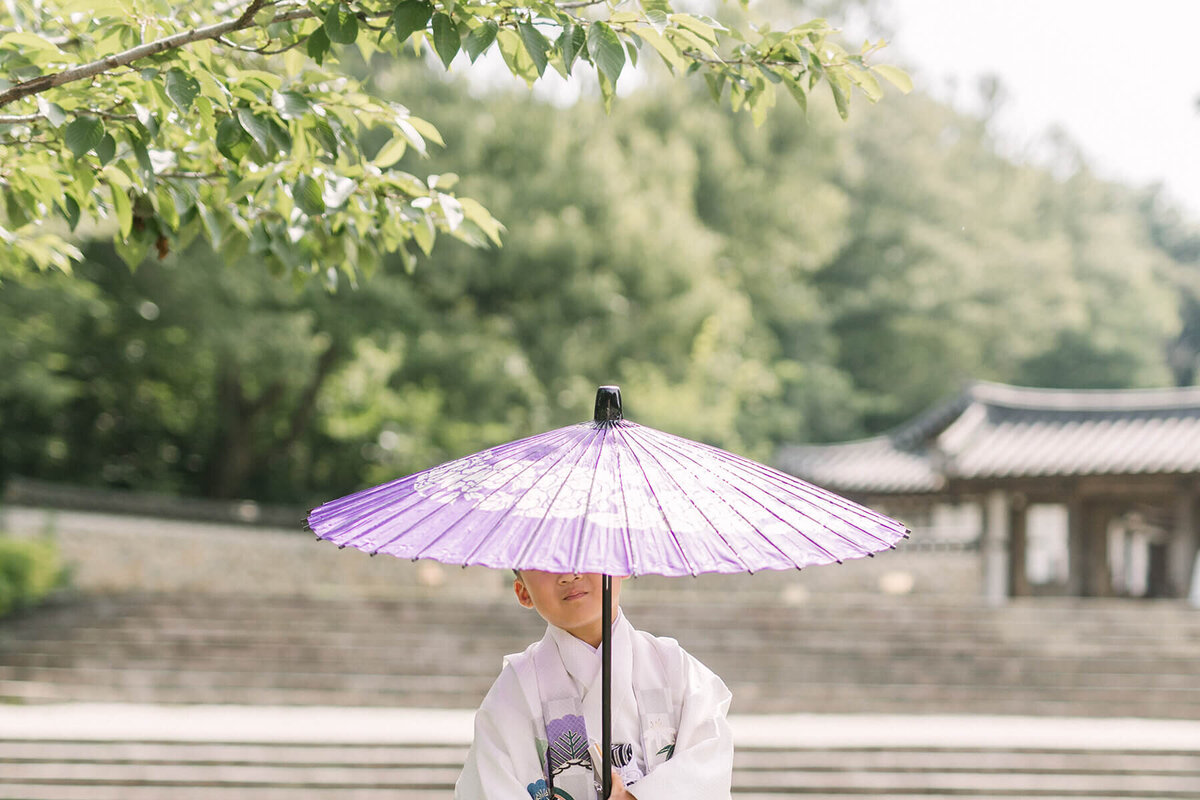 傘を深くかぶるようにして持っている5歳の男の子の七五三写真。袴の色と傘の紫色がマッチしていてオシャレな雰囲気。横浜市で撮影。