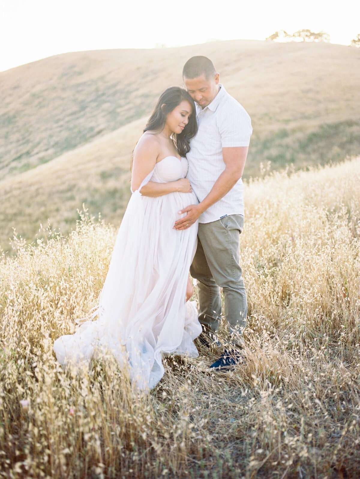 Pregnant woman and her husband framing her belly in a tulle dress taken by one of the top San Francisco Maternity Photographers Laurel Smith.