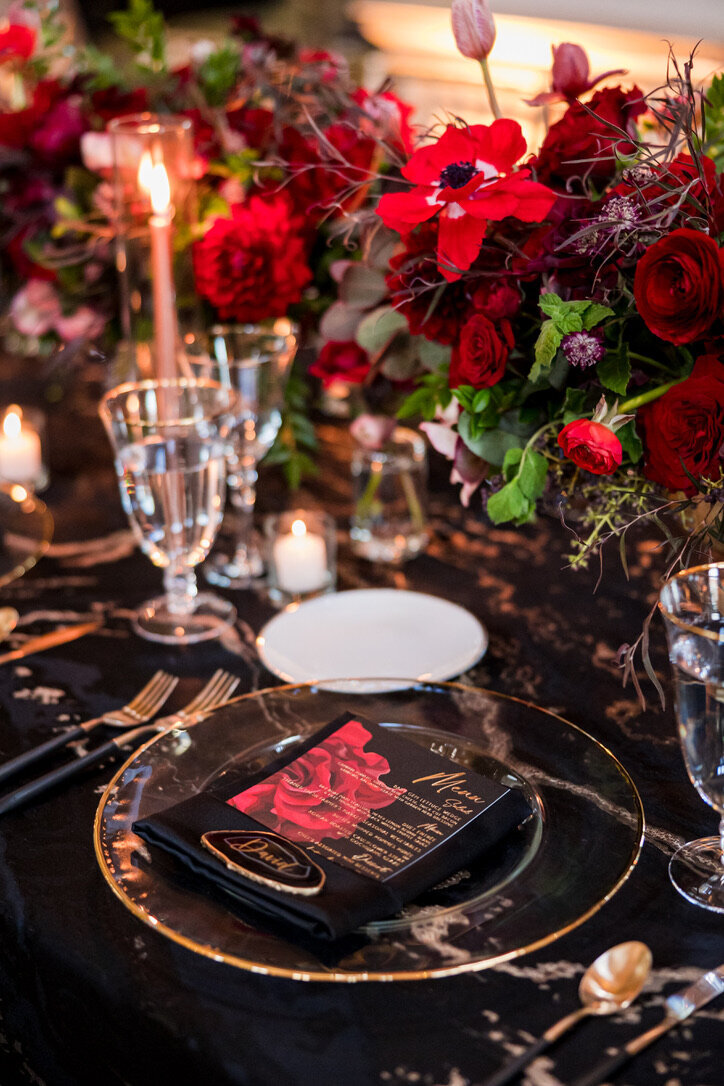 red roses, black and gold linen, gold charger, black napkin, taper candles, red roses