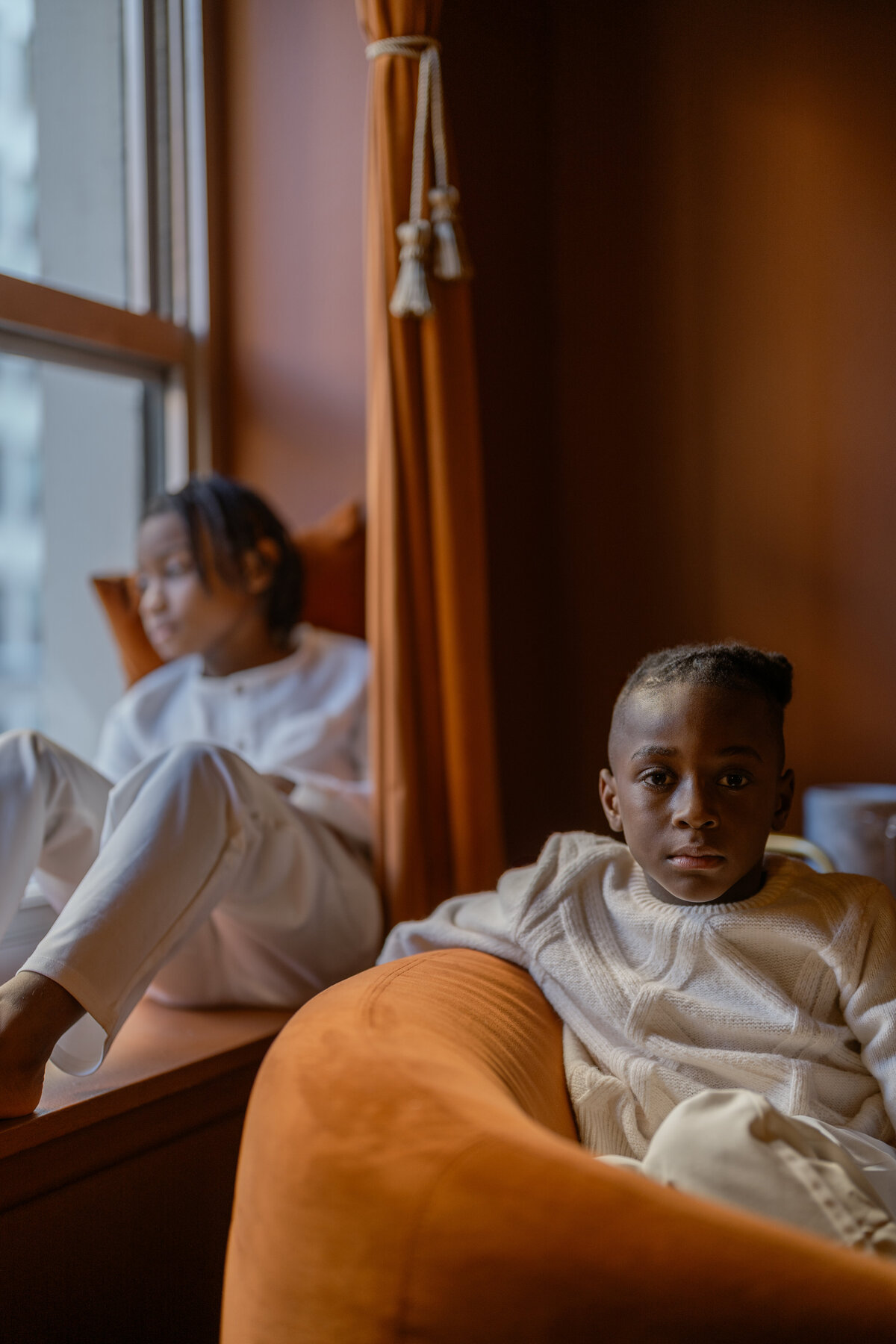 A fine art image of two children sitting comfortably on an orange couch, captured during an NYC family session, emphasizing warmth and familial bonds.