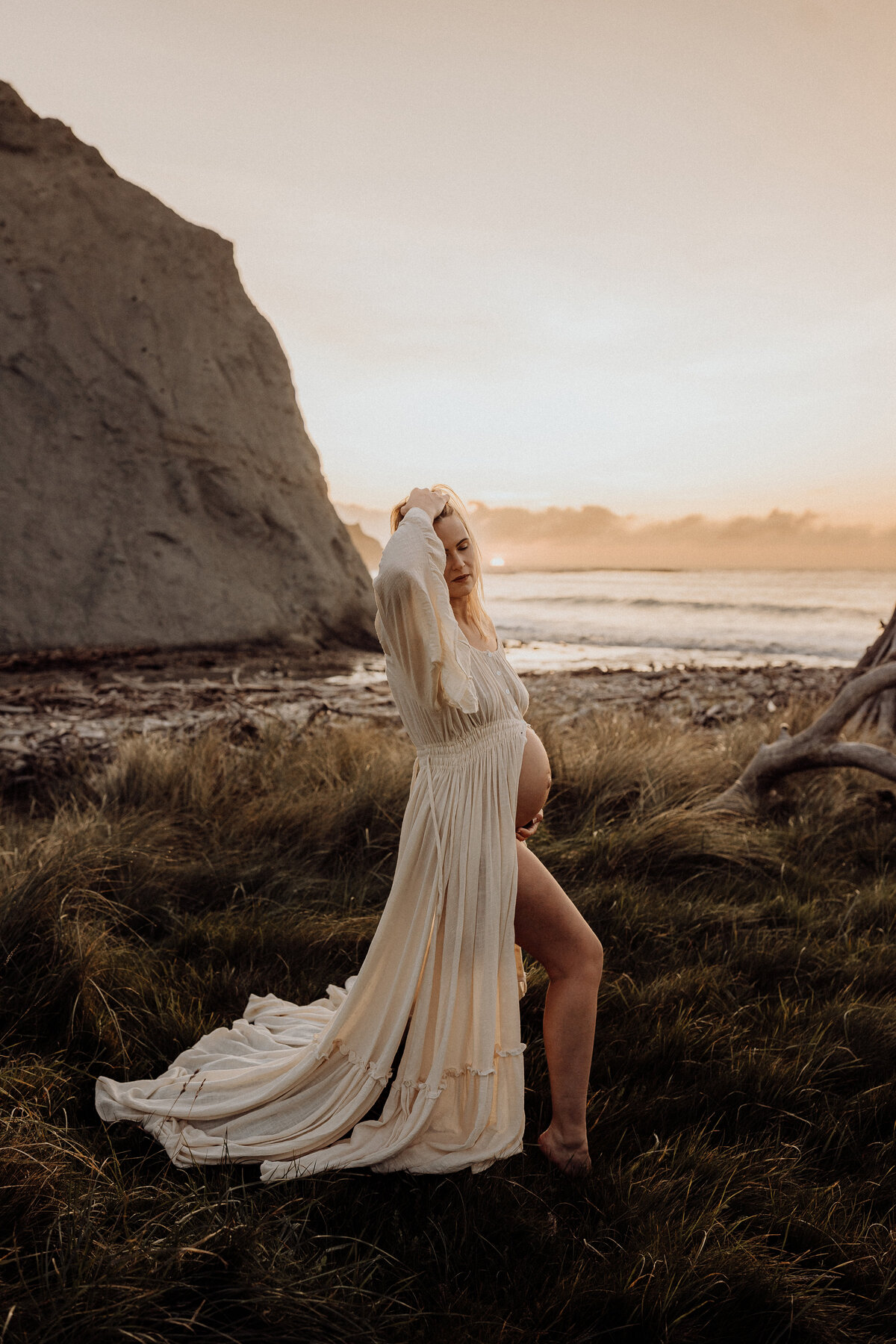 A mother to be posing for a maternity photographer during a sunset beach photoshoot in christchurch