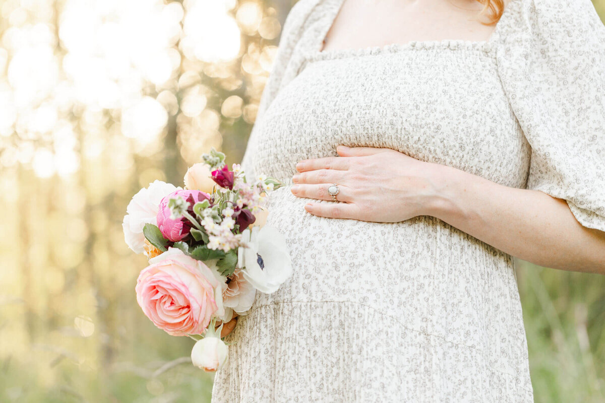 Woman holding her pregnant belly and a bouquet of flowers during her sunset maternity photo session in Portland, OR.