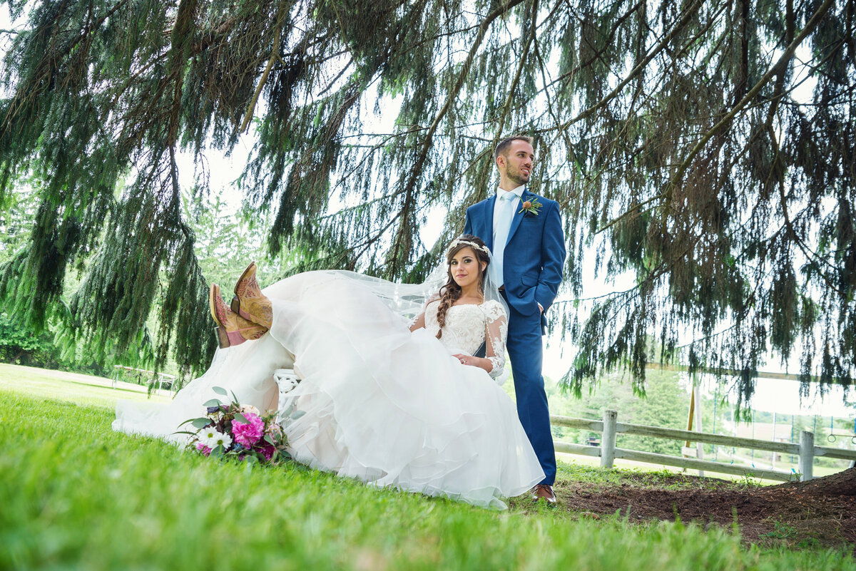 Bride wearing cowboy boots under willow tree.