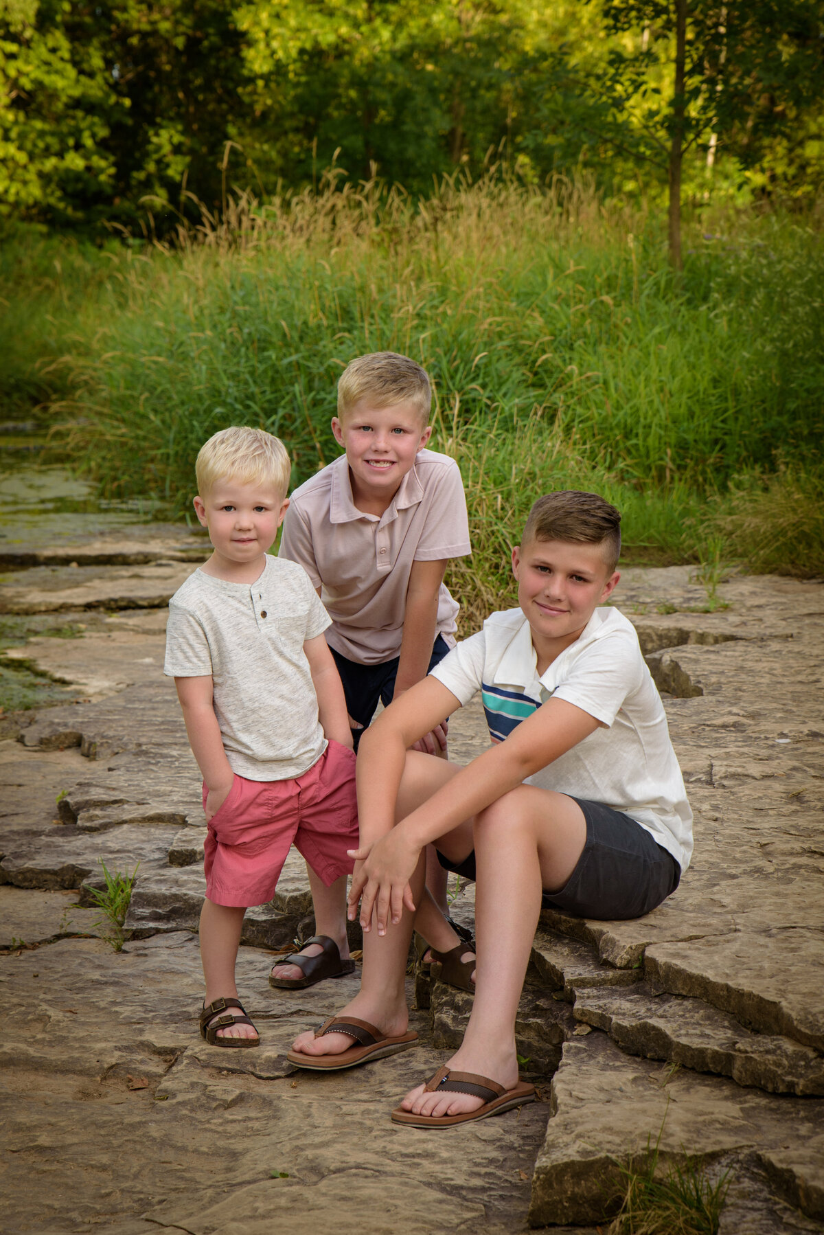 Sibling portrait of three young boys sitting on rocks near creek at Fonferek Glen County Park near Green Bay, Wisconsin
