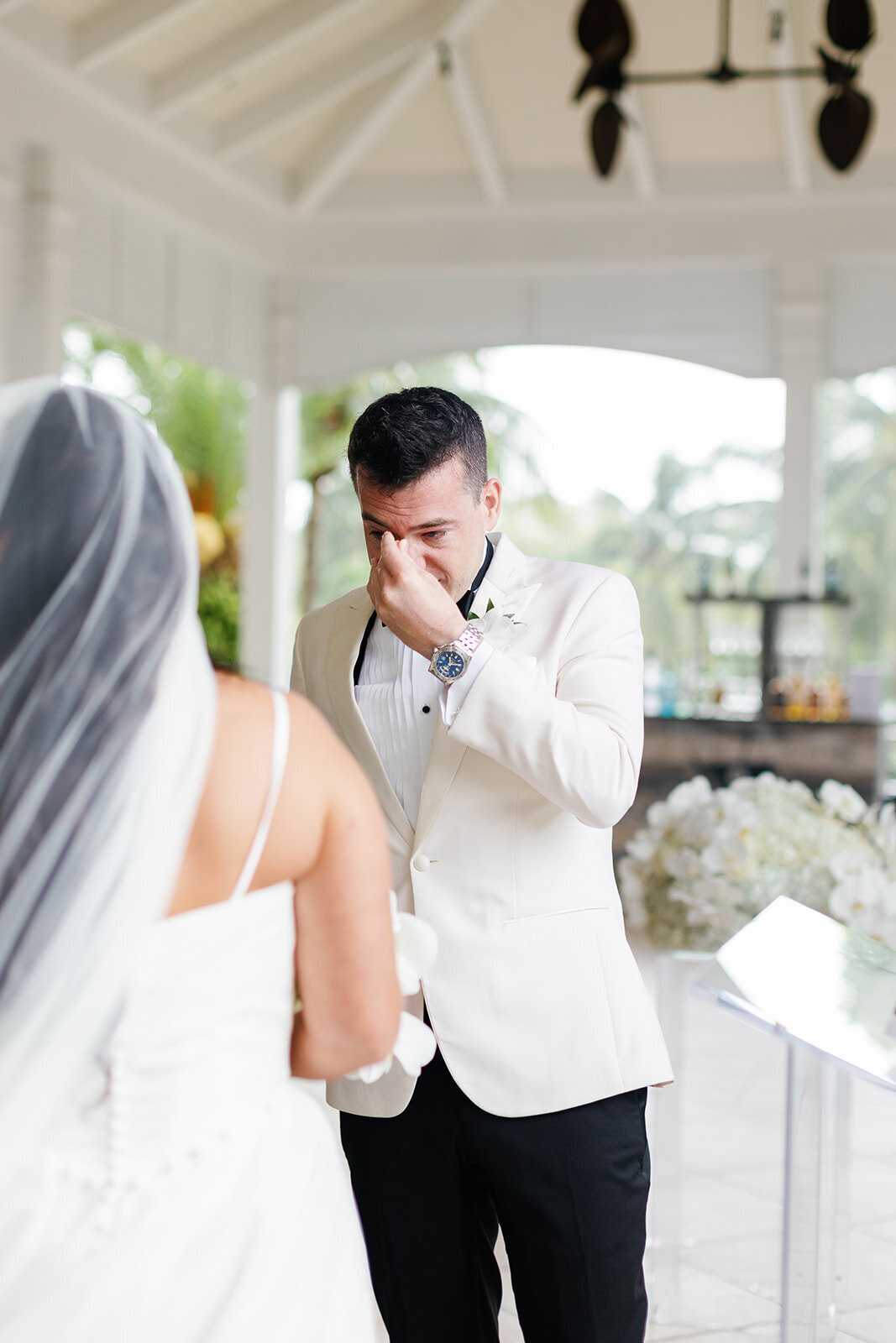 The groom wiping away tears during an emotional moment at the Ocean Reef wedding ceremony in Key Largo, captured by Claudia Amalia Photography.