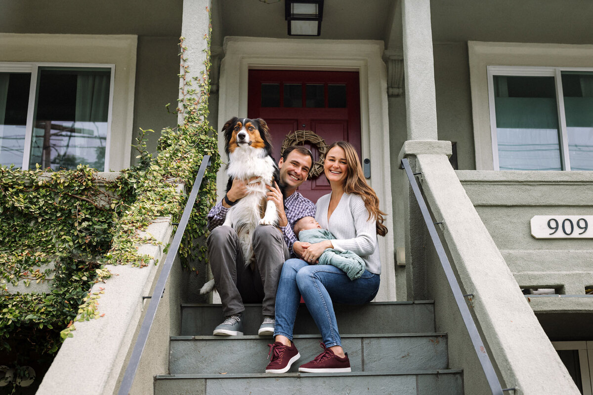 mom and dad sitting on front porch with newborn and large dog