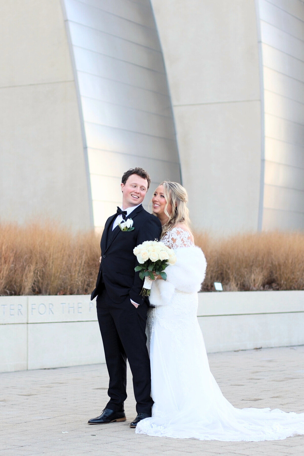 Winter bride and groom standing in front of Kauffman Center