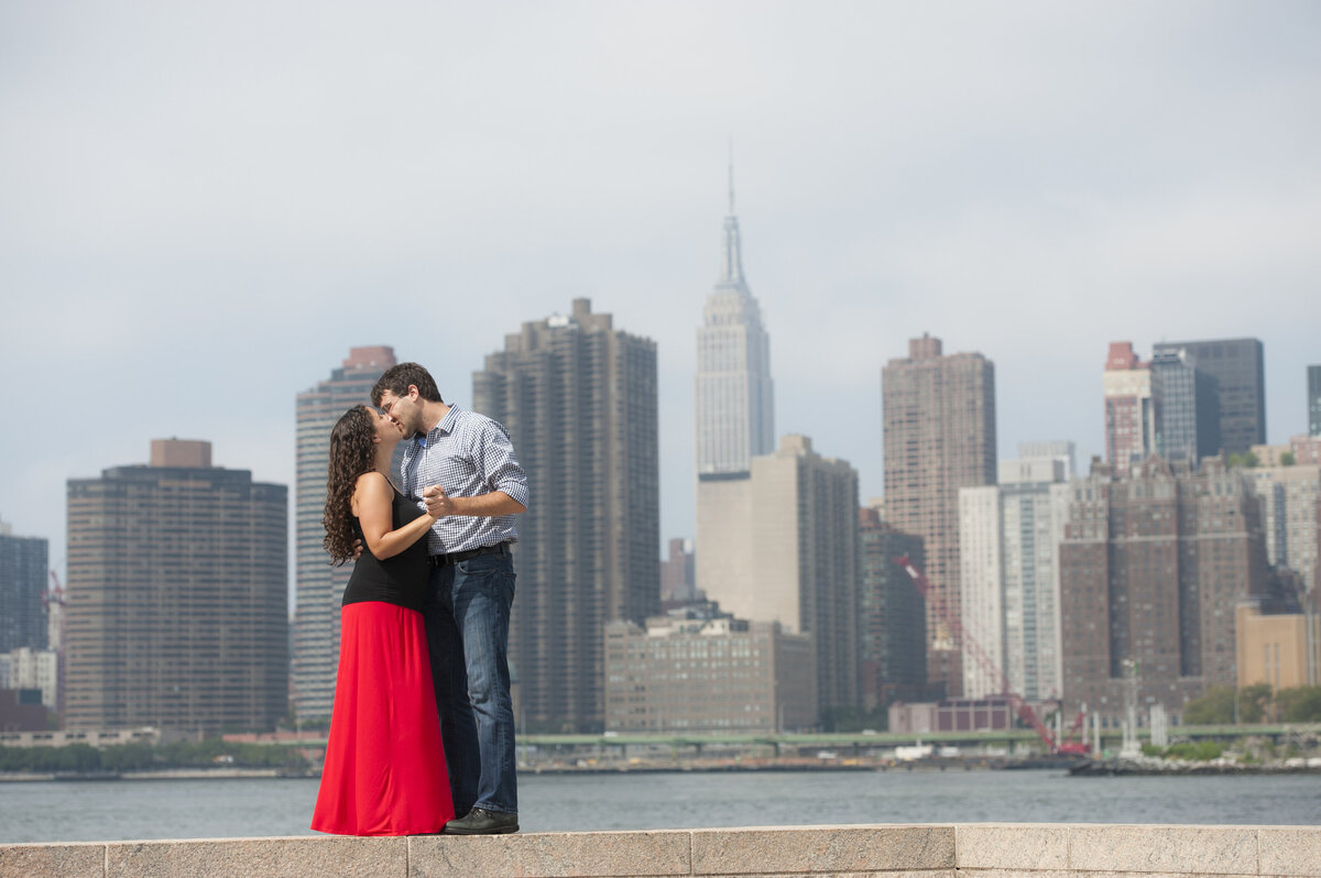 A couple kissing while holding hands with a city skyline behind them 