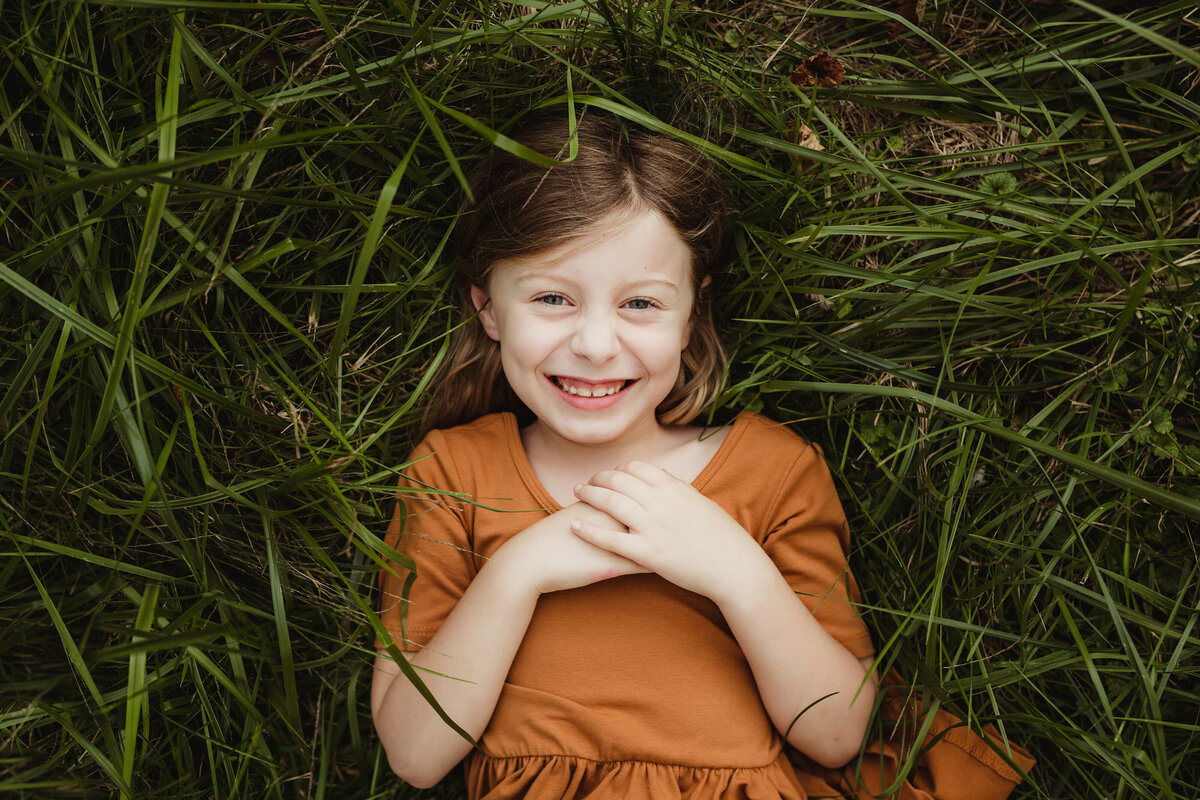 Young girl smiling and lying in tall grass.