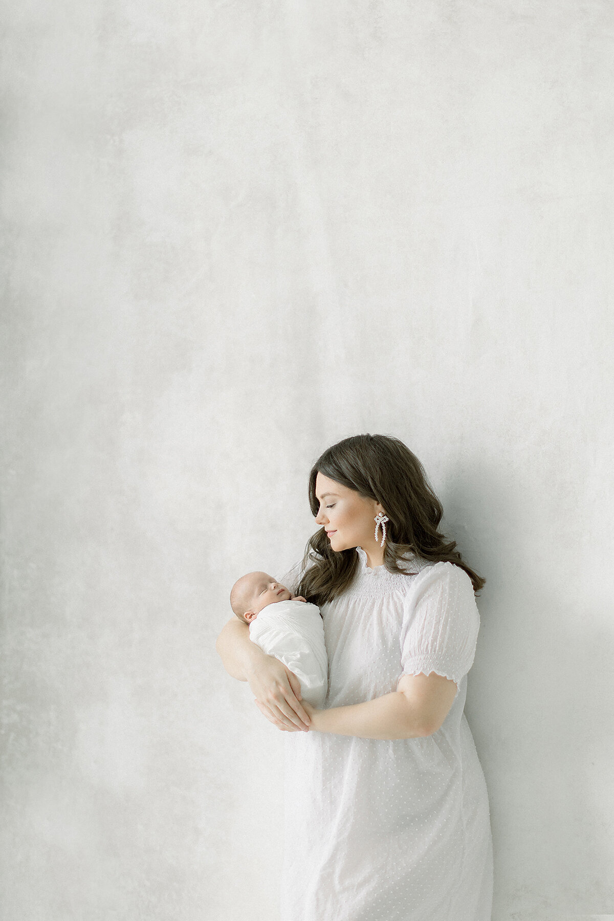 Newborn portrait of a new mother posing in front of a window for a studio family session at a photography studio located in the Dallas/Fort Worth area.